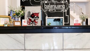 A reception desk with a black and white sign, framed pictures, and a vase with flowers. - Hotel O Monalisa Residence And Cafe (Padang)