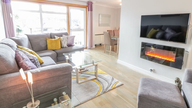 A modern living room with a grey sofa, a glass coffee table, and a flat-screen TV mounted on the wall. - Cumbrae View (Largs)
