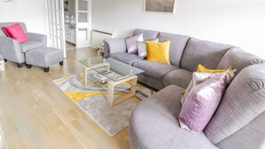 A modern living room with a grey sofa, a glass coffee table, and a wooden floor. - Cumbrae View (Largs)