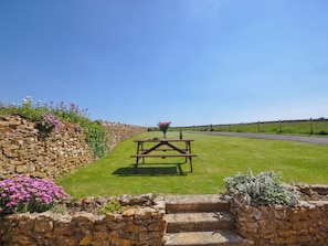 A stone wall with steps leading to a picnic table in a grassy area.