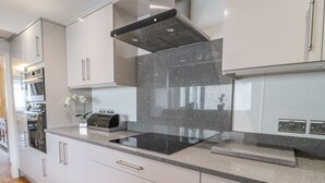 A modern kitchen with stainless steel appliances, a granite backsplash, and white cabinetry. - Beach Cove View (Newbiggin-by-the-Sea)