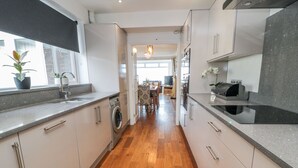 A modern kitchen with a central island, wooden flooring, and built-in appliances. - Beach Cove View (Newbiggin-by-the-Sea)
