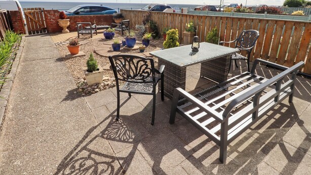 A patio with a table and chairs, surrounded by potted plants and a view of the sea. - Beach Cove View (Newbiggin-by-the-Sea)