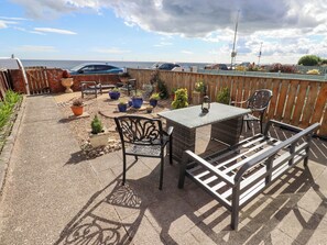 A patio with a table and chairs, surrounded by potted plants and a view of the sea. - Beach Cove View (Newbiggin-by-the-Sea)