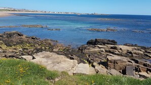 A coastal landscape with rocky terrain and clear blue waters. - Beach Cove View (Newbiggin-by-the-Sea)