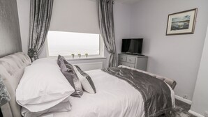 A bedroom with a bed, a television, and a window with curtains. - Beach Cove View (Newbiggin-by-the-Sea)