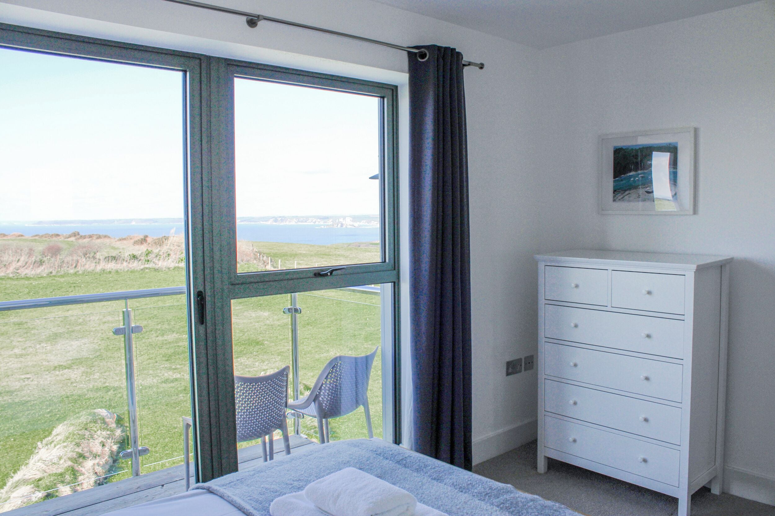 A bedroom with a large window, a white dresser, and a chair by the window.