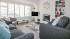 A modern living room with a fireplace, a flat-screen TV, and a bookshelf. - Bayview (St Austell)