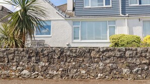 A two-story house with a stone wall in front, a palm tree, and a window with shutters. - Bayview (St Austell)