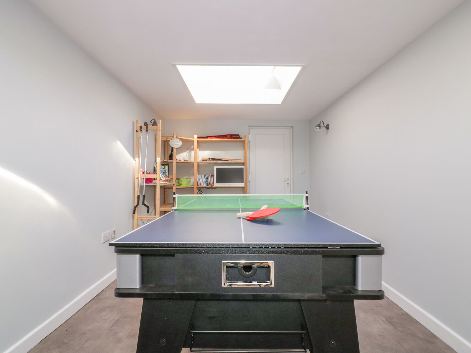 A ping pong table in a room with a skylight, a bookshelf, and a door.