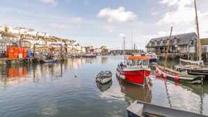 A harbor with boats docked, a small boat in the foreground, and buildings along the water's edge. - Bayview (St Austell)