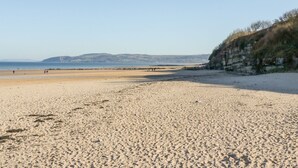 Ein weiter Sandstrand mit blauem Himmel und sanften Hügeln in der Ferne.