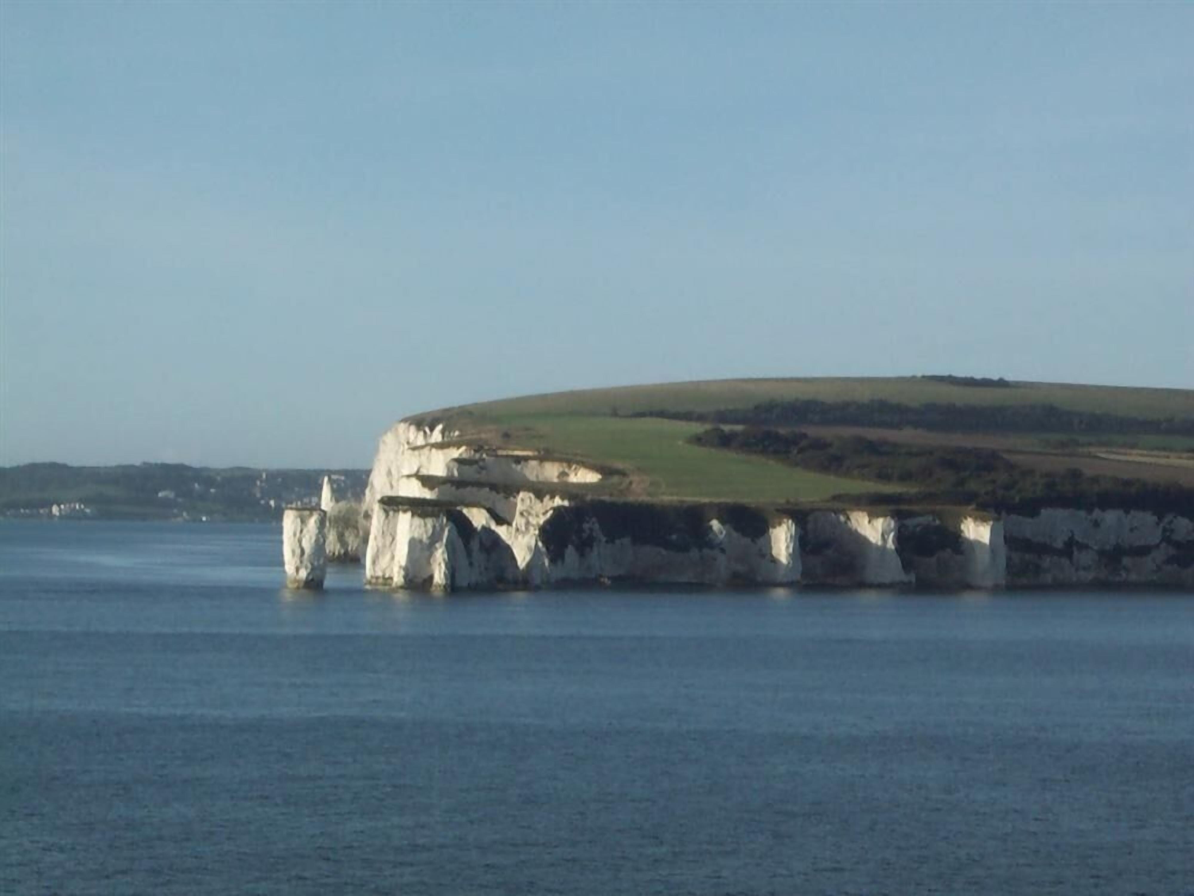A coastal landscape with white cliffs and a green hill in the background.