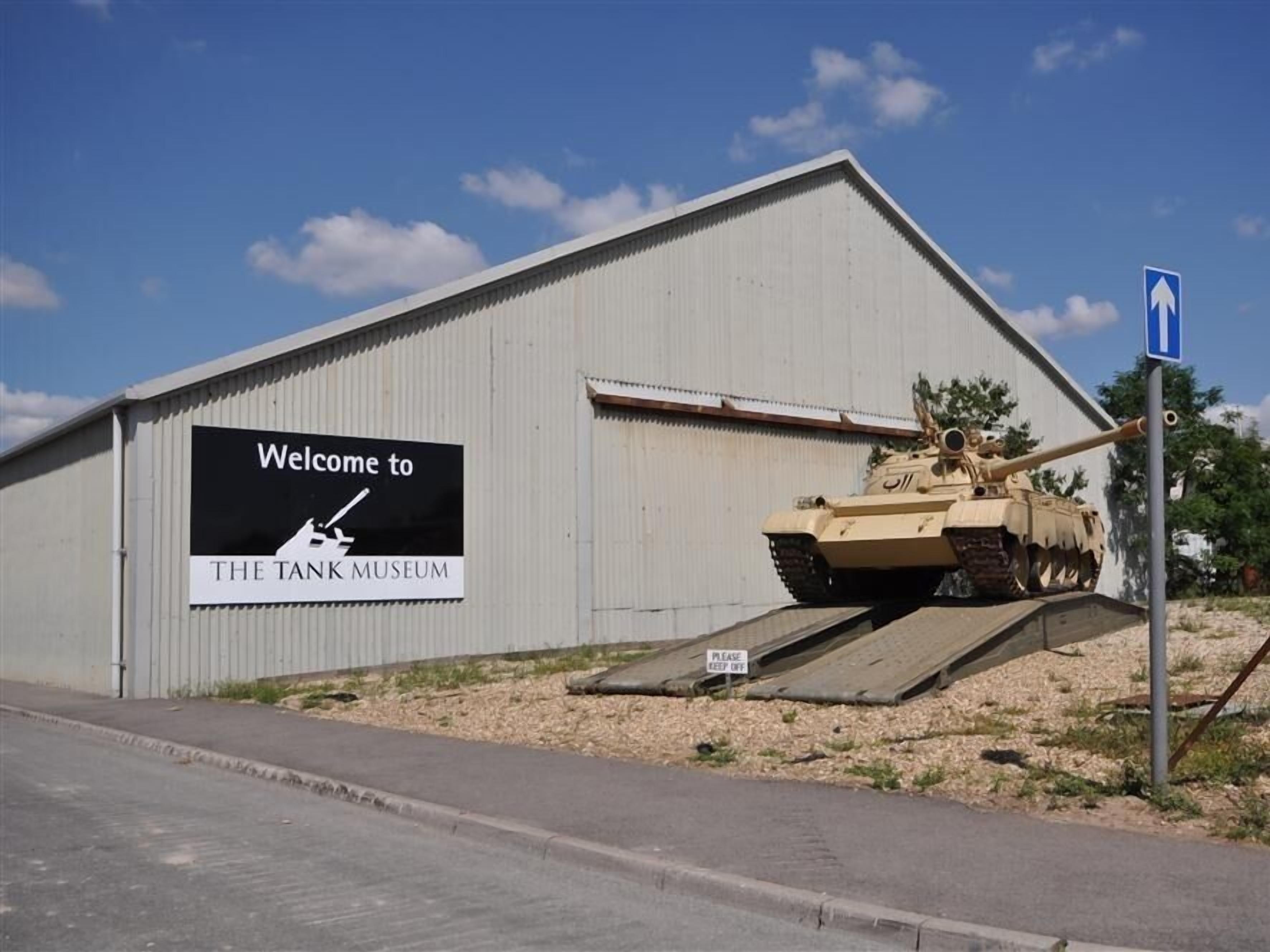 A building with a sign welcoming visitors to the Tank Museum, featuring a military tank outside.