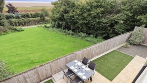 A patio with a table set for four, surrounded by a wooden fence and a grassy lawn. - Shore View (Grange-over-Sands)