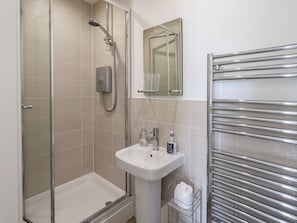 Un baño moderno con ducha envuelta en vidrio, lavamanos pedestal y toallero.