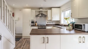 A modern kitchen with white cabinets, a central island, stainless steel appliances, and a window with flowers. - Shore View (Grange-over-Sands)