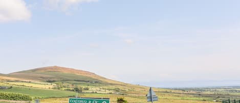 A rural landscape with a green sign indicating a parking area and a view of rolling hills in the distance.