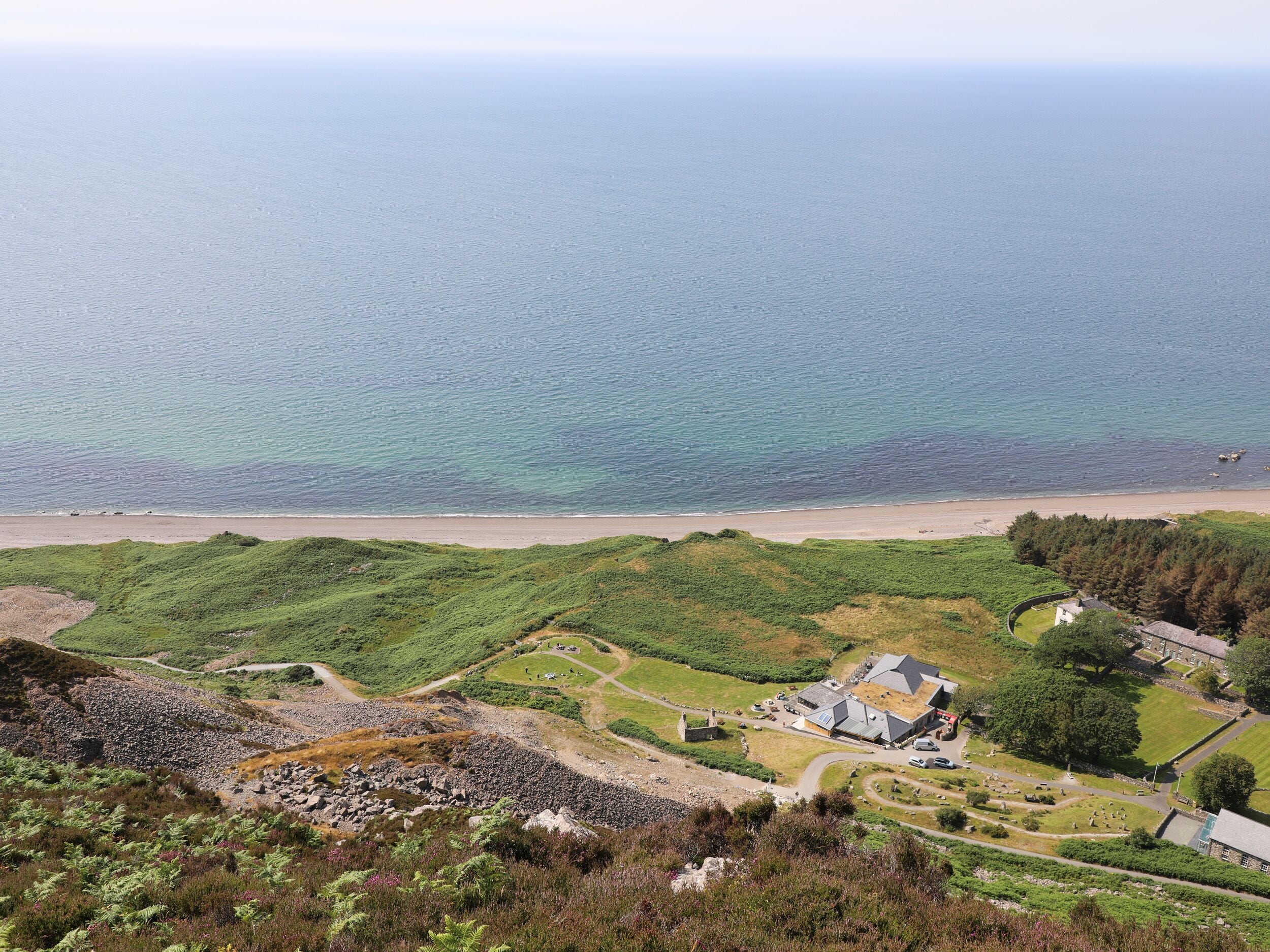 A coastal landscape with a beach, grassy hills, and a small village with buildings and a cemetery.