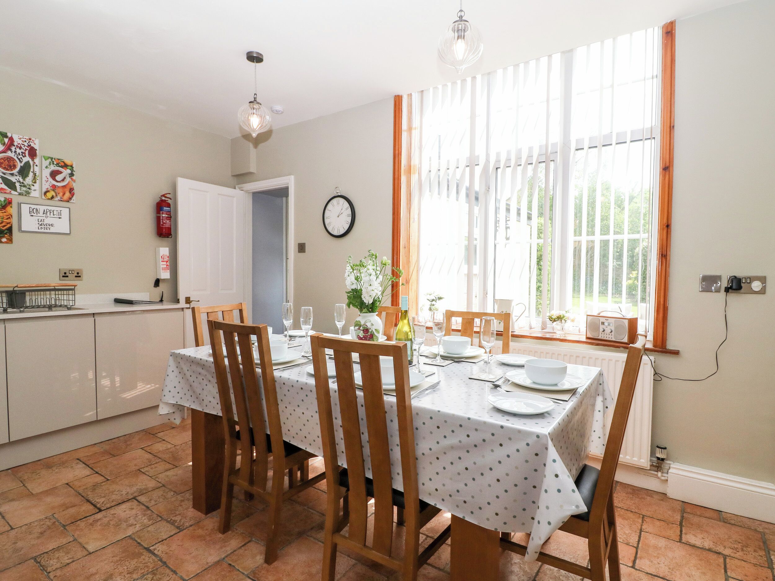 A dining area with a table set for four, wooden chairs, a white tablecloth, and a window with curtains.