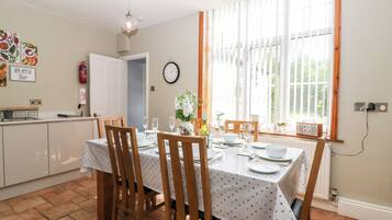 A dining area with a table set for four, wooden chairs, a white tablecloth, and a window with curtains.