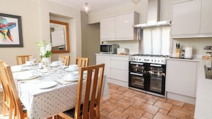 Une cuisine moderne avec des meubles blancs, une cuisinière à gaz, un four et un four à micro-ondes. On y trouve une table à manger mise avec des assiettes et des verres.