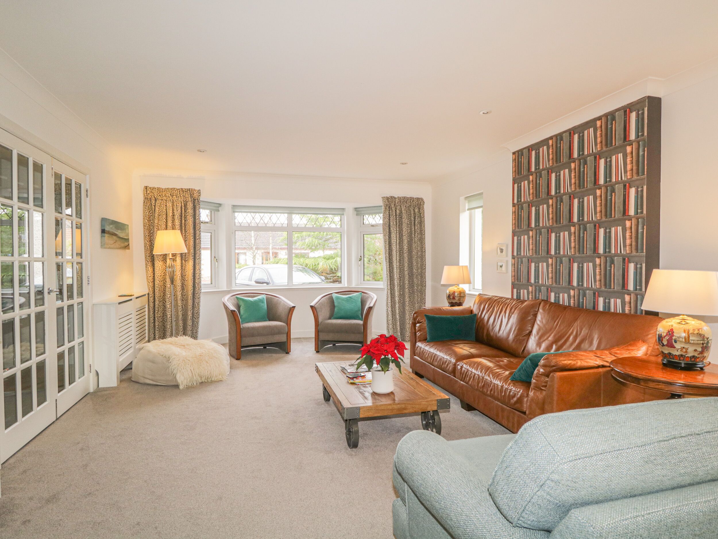 A living room with a brown leather sofa, two armchairs, a coffee table, and a bookshelf filled with books.