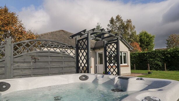 A hot tub with a wooden deck and a pergola structure.