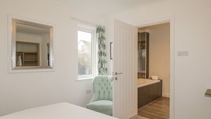 A bedroom with a bed, a chair, a window, a mirror, and a door leading to a bathroom.