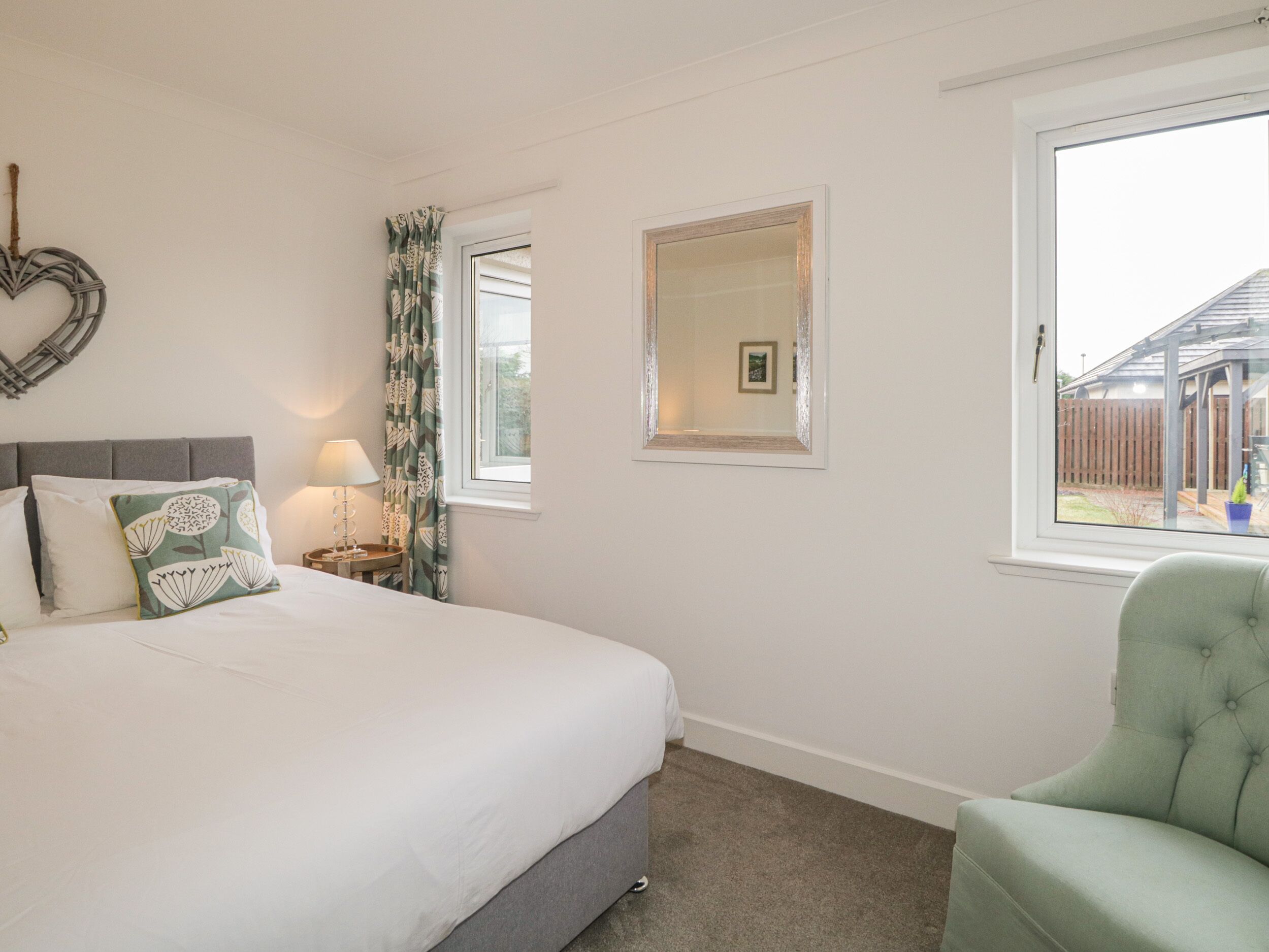 A bedroom with a bed, a nightstand, a lamp, a mirror, and a window.
