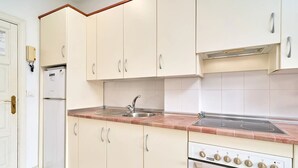 Une cuisine avec des meubles blancs, un évier à deux bacs, une cuisinière et un réfrigérateur.