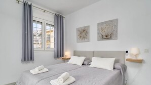 Une chambre à coucher avec un lit, deux oreillers, une table de chevet avec une lampe et des œuvres d’art accrochées au mur.