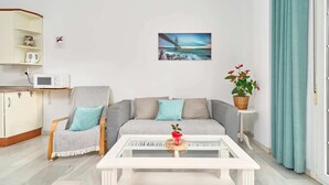 Un salon comprenant un canapé, une table basse, un four à micro-ondes, un meuble, un tableau et une plante.