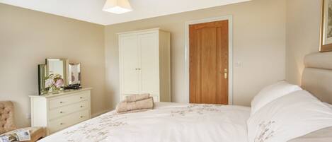 A bedroom with a large bed, a wardrobe, a wooden door, and a small table with a chair.
