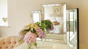 Um quarto com uma cama, uma mesa de cabeceira com um vaso de flores e três espelhos na parede.