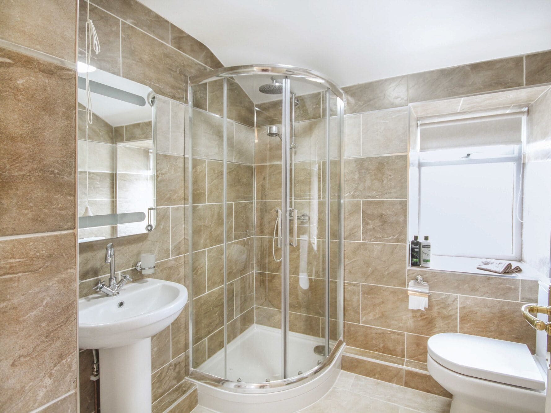 Un baño moderno con ducha de vidrio, lavamanos pedestal y retrete.