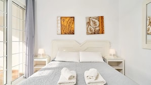 Ein Hotelzimmer mit einem großen Bett, zwei Nachttischen, einem Fenster mit Vorhängen und zwei Wandbildern.