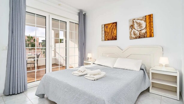 Ein Schlafzimmer mit einem großen Bett, zwei Nachttischen, einem Balkon mit Schiebetüren und zwei Wandbildern.