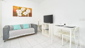 Ein modernes Wohnzimmer mit grauem Sofa, einem Flachbildfernseher, einem Esstisch mit Stühlen und zwei an der Wand befestigten Blumenbildern.