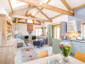 A cozy, rustic interior with exposed wooden beams, a dining area with a table and chairs, a kitchen with cabinets, and a living area with a sofa and a TV. - Little Willow (Blandford Forum)