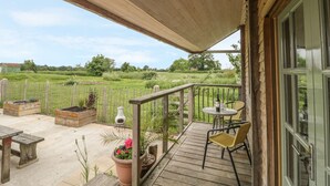 Terraza de madera con una mesa y sillas, con vistas a un campo cercado.