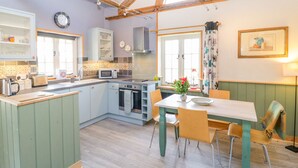 Una cocina compacta con una isla central, un comedor con mesa y sillas, y una ventana con cortina.