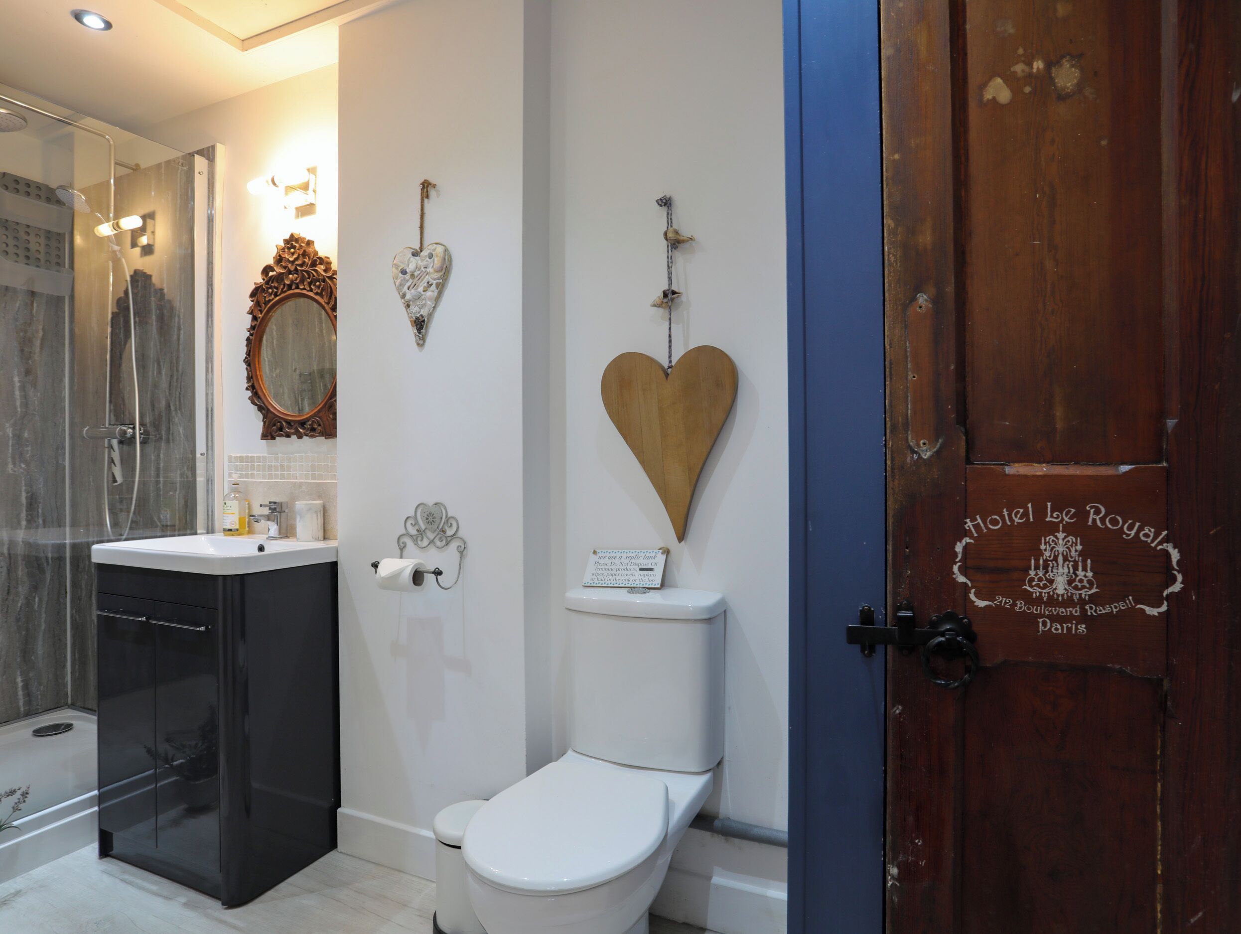 A bathroom with a shower, toilet, and vanity. There are decorative heart-shaped items on the wall.