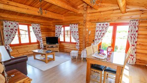 Eine Blockhütte mit Holzvertäfelung, einem Fernseher, einem Esstisch und einem Sofa.