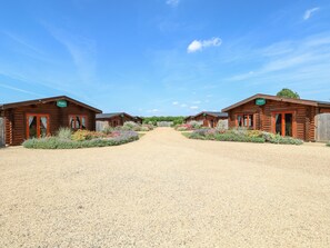 A row of log cabins with gravel paths and flower beds in front. - Ash Lodge (Oakham)
