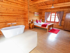 A log cabin bedroom with a wooden bed, a white bathtub, and a red rug. - Ash Lodge (Oakham)