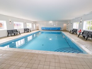 An indoor swimming pool with tiled flooring, benches along the sides, and windows allowing natural light. - Ash Lodge (Oakham)