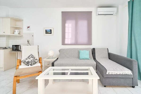 A modern living room with a sofa, a coffee table, a side table, and a kitchen area with a kettle and a microwave.