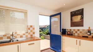 A modern kitchen with a blue door, a sink, and a countertop with a bottle of champagne. - Firkin Cottage (Weymouth)
