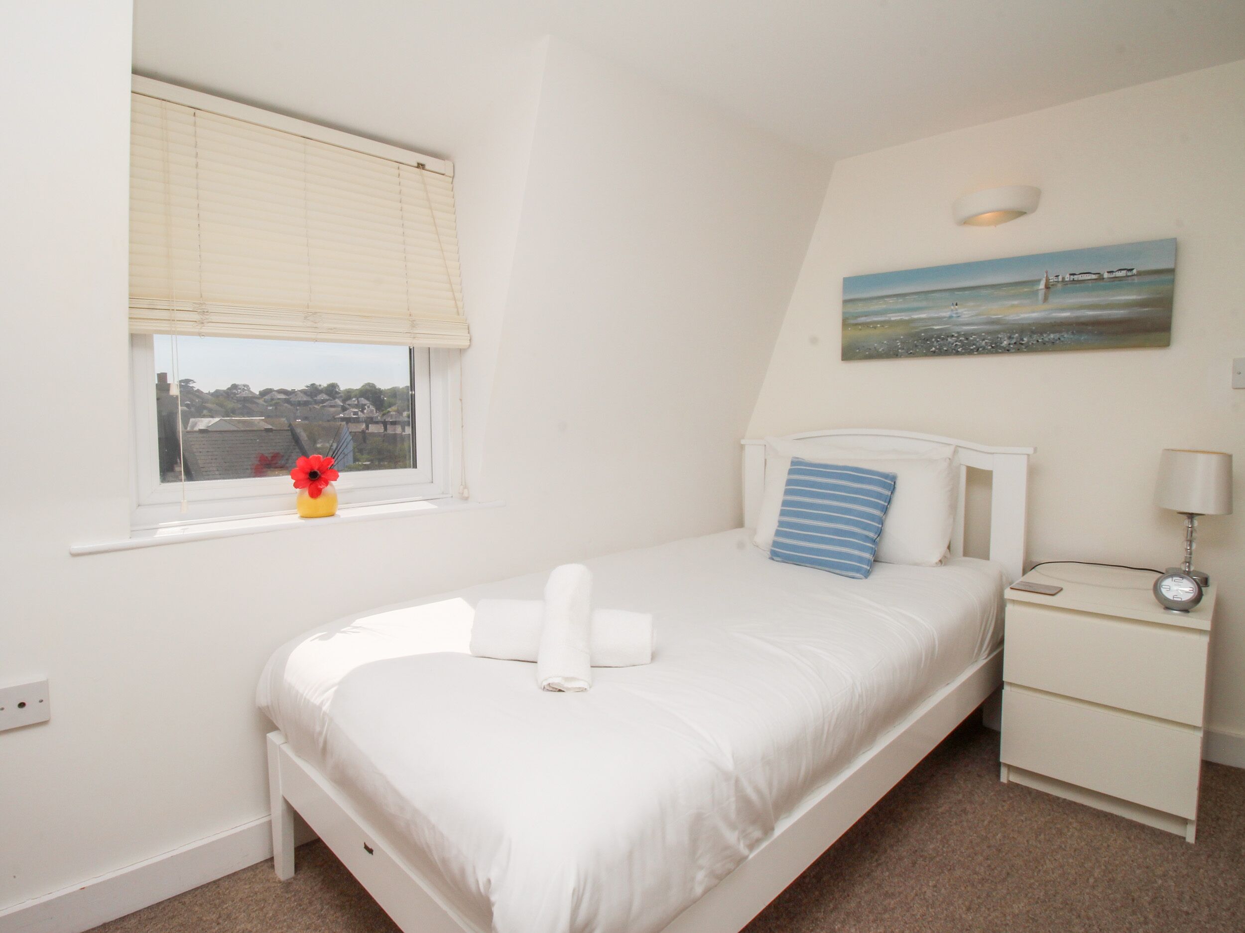 A bedroom with a bed, a nightstand, a lamp, a painting, and a window with blinds.